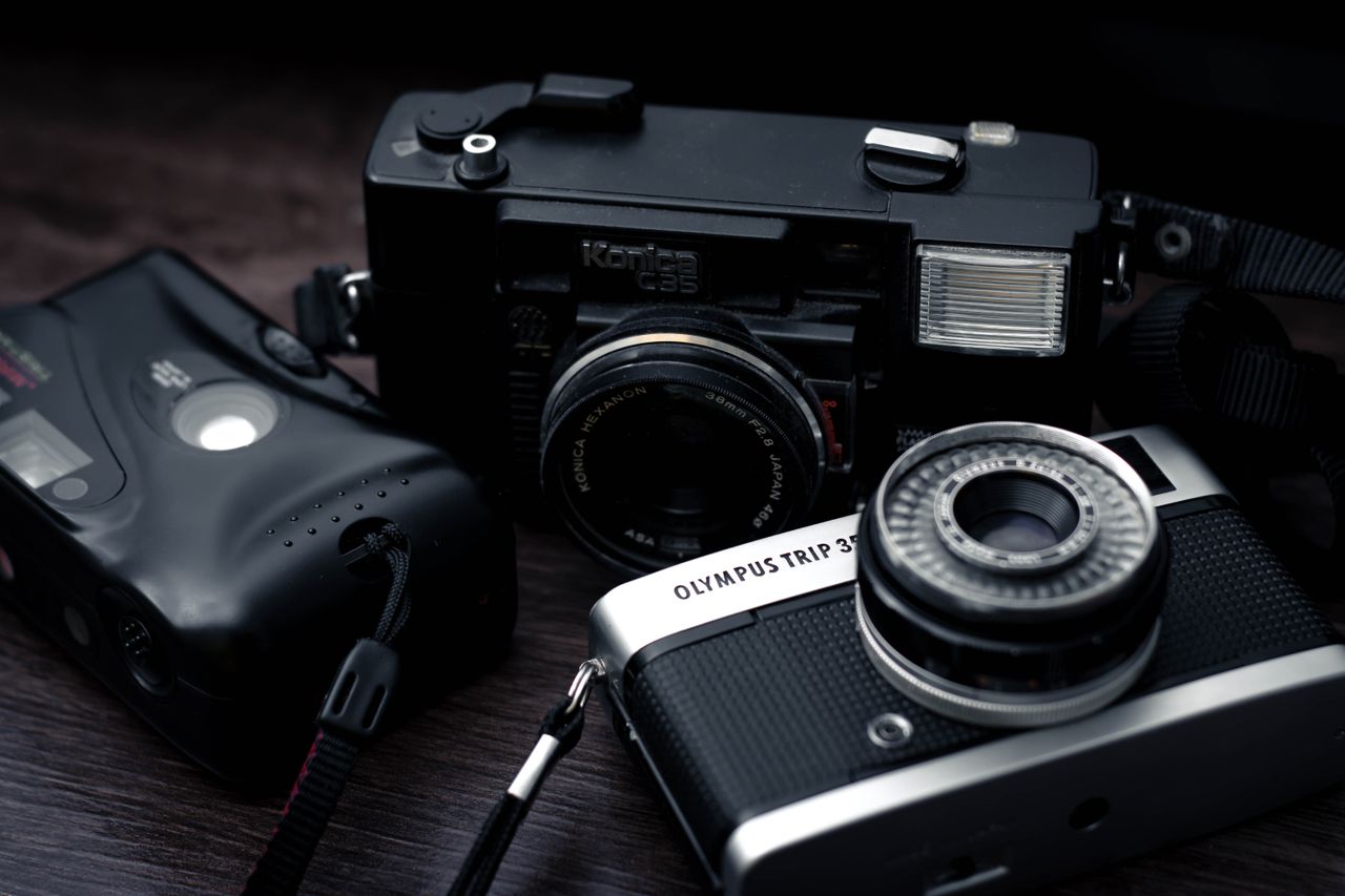 A set of vintage cameras including Olympus and Konica models on a wooden surface.